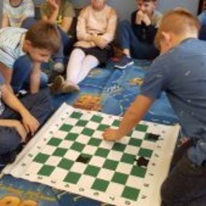 trzy osoby z klasy 2c grają w szachy a reszta klasy siedzi w kole i obserwuje.jpg