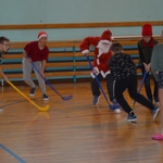 uczniowie przebrani za mikołajów grają w hokeja na sali.jpg