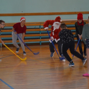 uczniowie przebrani za mikołajów grają w hokeja na sali.jpg
